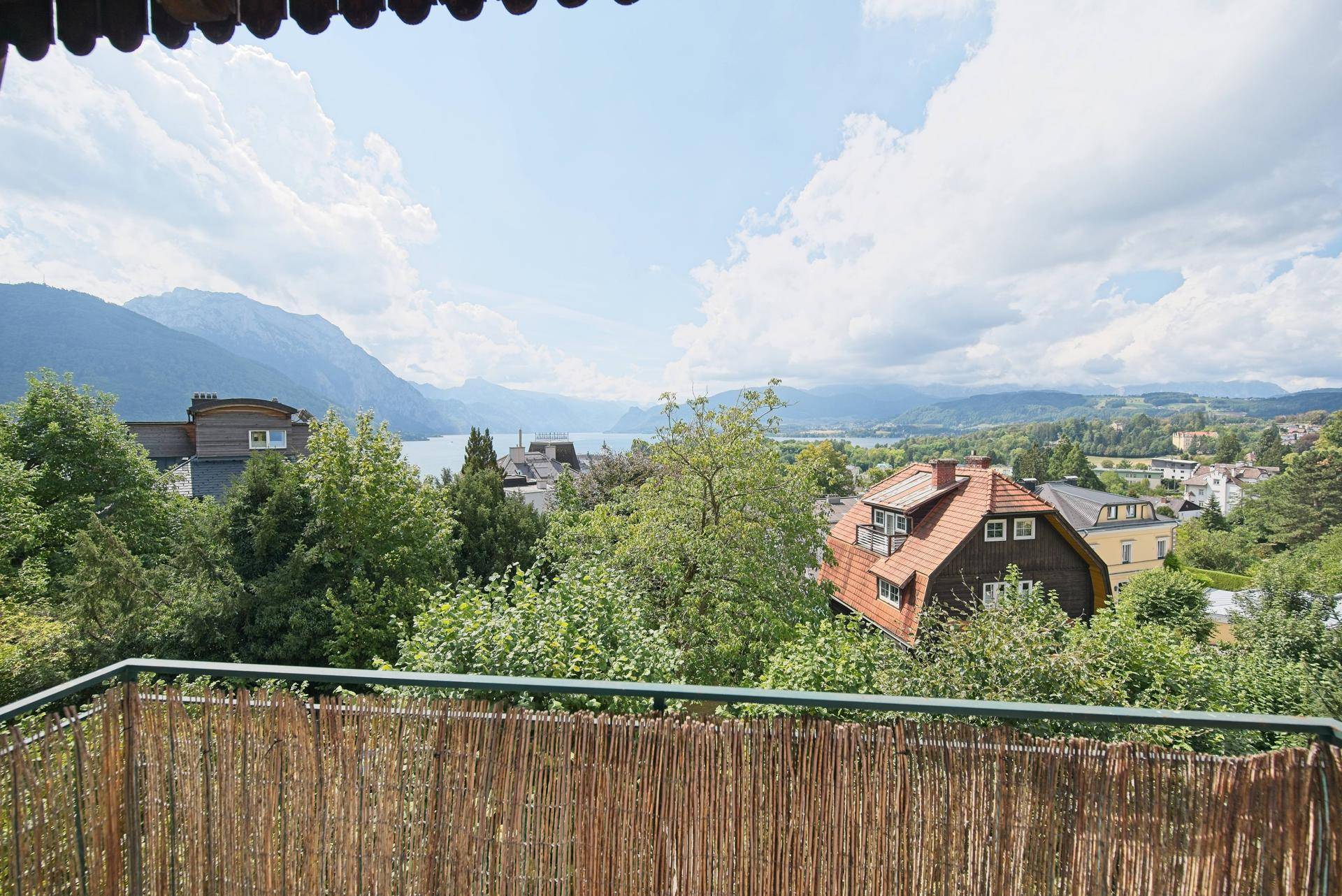 Panoramablick von einem Balkon auf einen See, Berge und die umliegende grüne Landschaft.