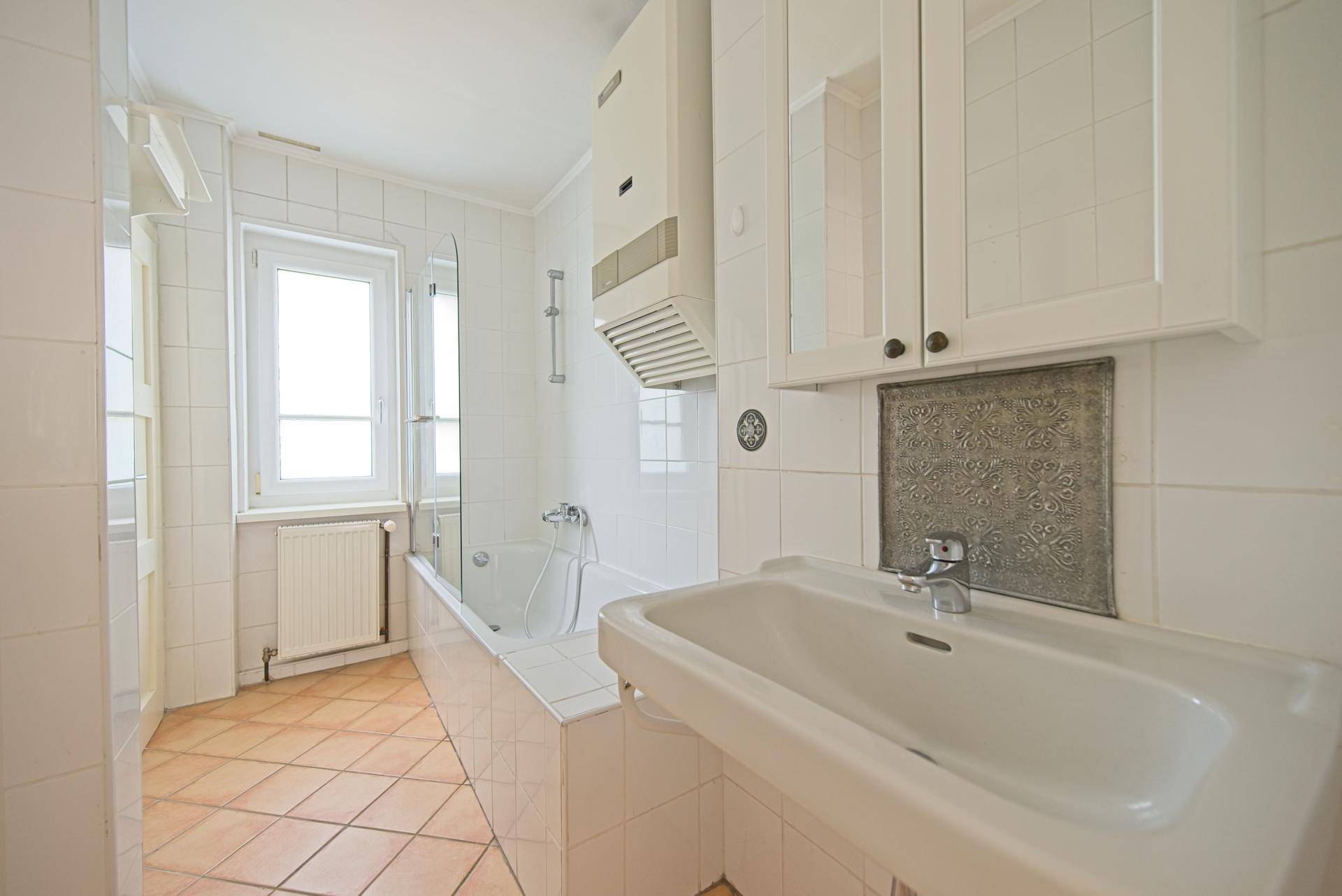Gefliestes Badezimmer mit Badewanne, Waschbecken und Fenster, in einem traditionellen Stil.