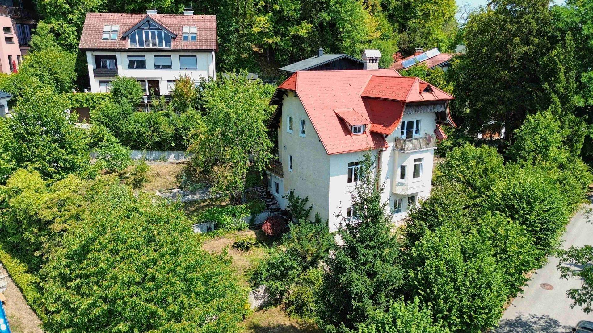 Weitläufige Luftaufnahme eines Hauses mit rotem Dach, umgeben von Bäumen und einer ruhigen Straße.