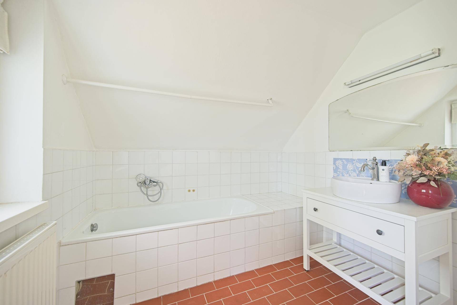 Helles Badezimmer im Dachgeschoss mit Badewanne, Waschbecken und schrägen Wänden.