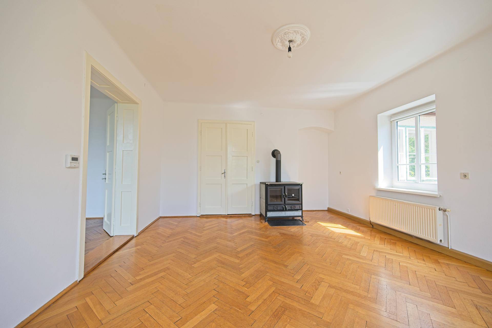 Helles Zimmer mit Fischgrätparkett und einem gemütlichen Holzofen, ideal für kalte Tage.