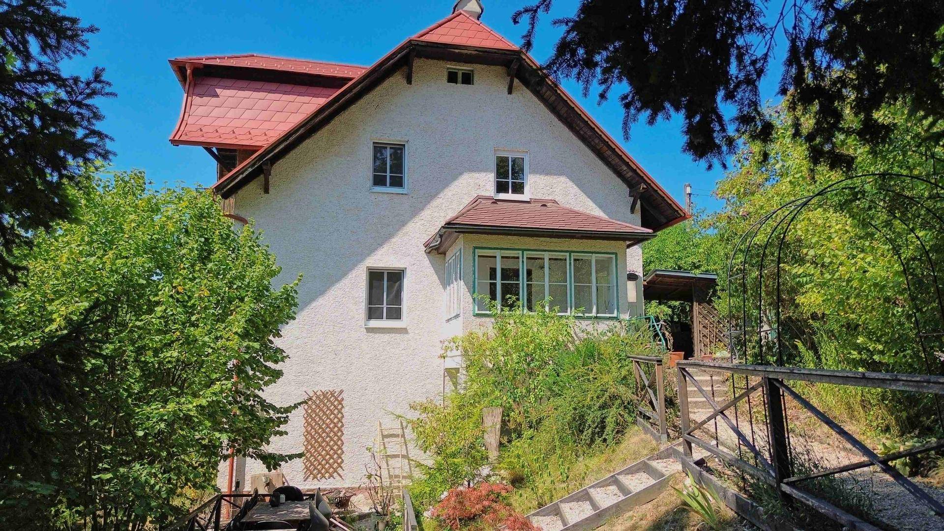 Seitenansicht des Hauses mit einem charmanten Wintergarten und üppiger grüner Bepflanzung im Gartenbereich.