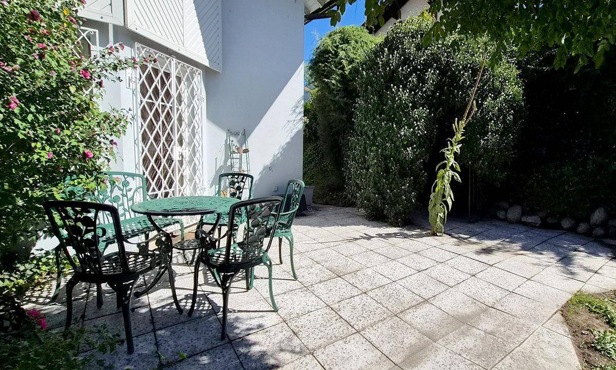 Gepflasterte Terrasse mit grünen Gartenmöbeln, umgeben von Rosenbüschen und Hecken.
