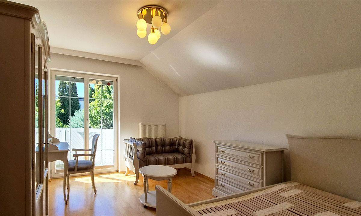 Schlafzimmer mit Holzparkettboden, hellen Möbeln und Zugang zu einem Balkon.