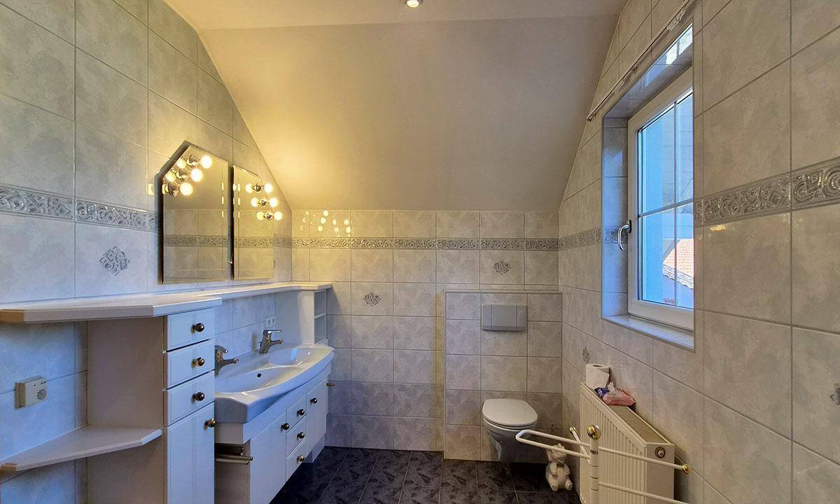 Badezimmer mit hellen Fliesen, Waschtisch, Toilette und einem Fenster für Tageslicht.