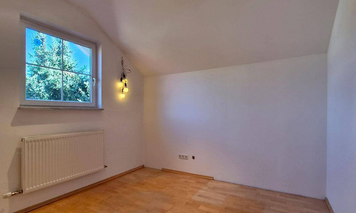 Helles Zimmer mit Holzparkettboden, weißen Wänden und einem Fenster mit Blick auf Bäume.