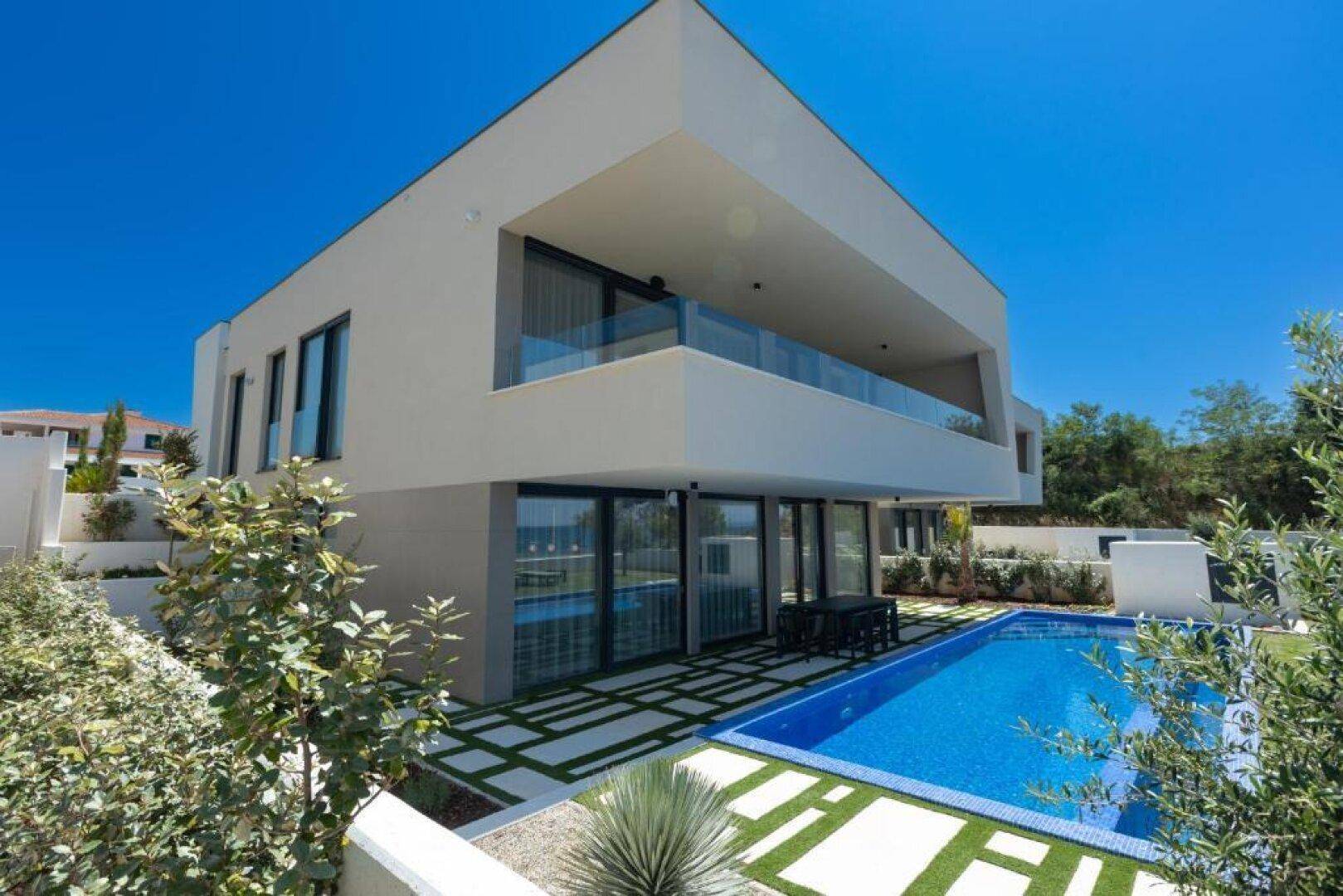 Moderne Villa mit klaren Linien, großem Pool und gepflegtem Gartenbereich unter blauem Himmel.