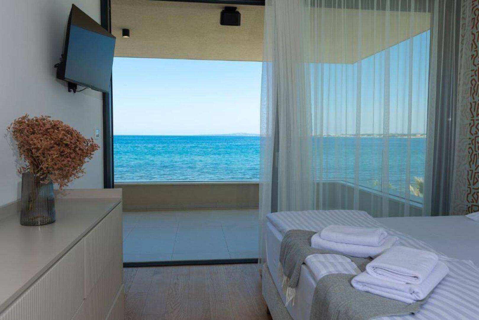 Schlafzimmer mit Doppelbett und raumhohen Fenstern, die einen atemberaubenden Blick auf das Meer bieten.