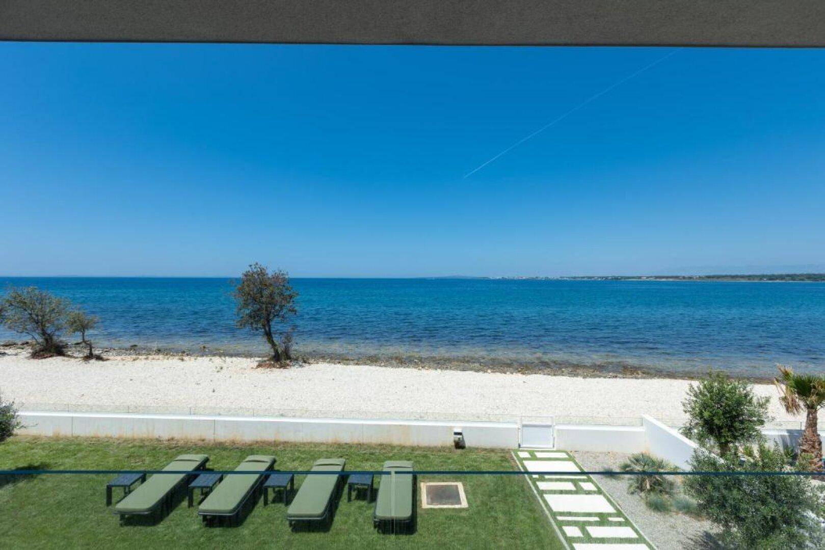 Gepflegter Gartenbereich mit Liegestühlen, Pool und atemberaubendem Blick auf das Meer und den Strand.