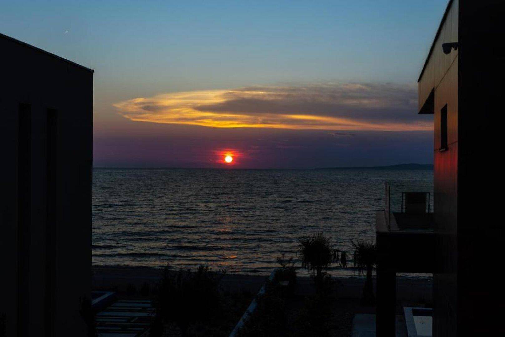 Spektakulärer Sonnenuntergang über dem Meer, eingerahmt von den modernen Gebäuden der Anlage.