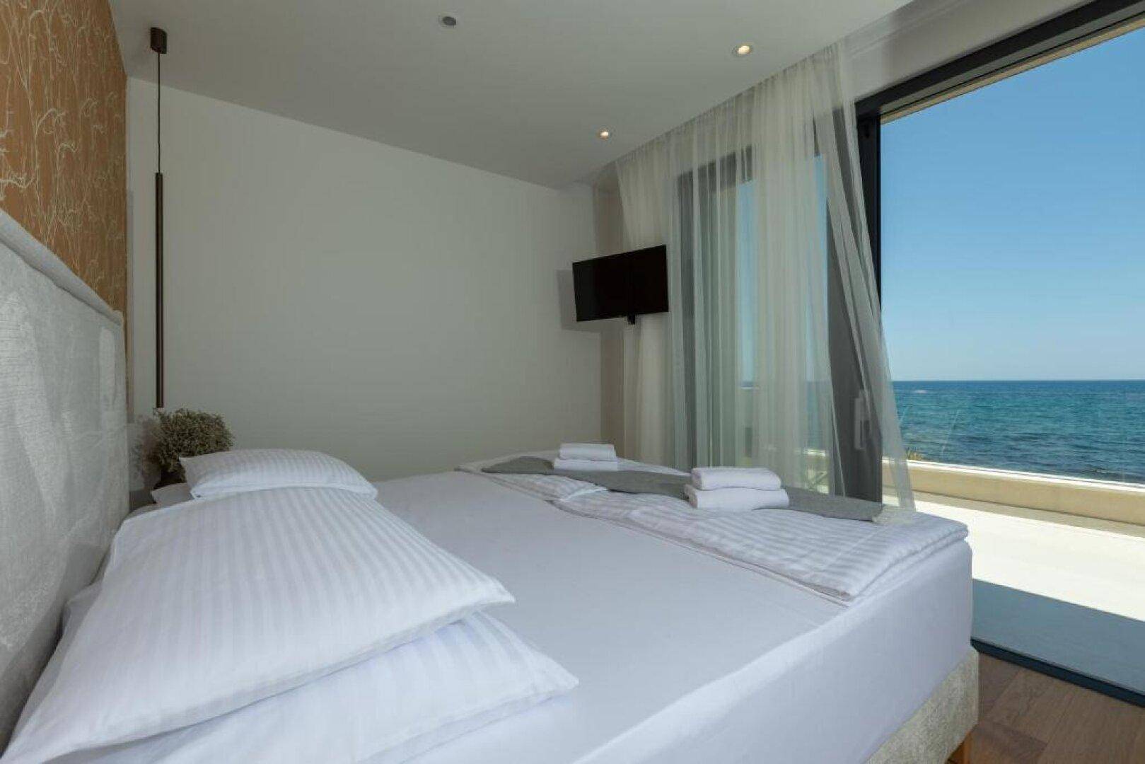 Helles Schlafzimmer mit großem Bett, Meerblick und Zugang zu einem Balkon.