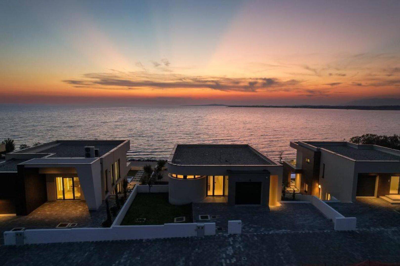 Beeindruckende Abendstimmung über modernen Villen am Meer mit beleuchteten Innenhöfen.