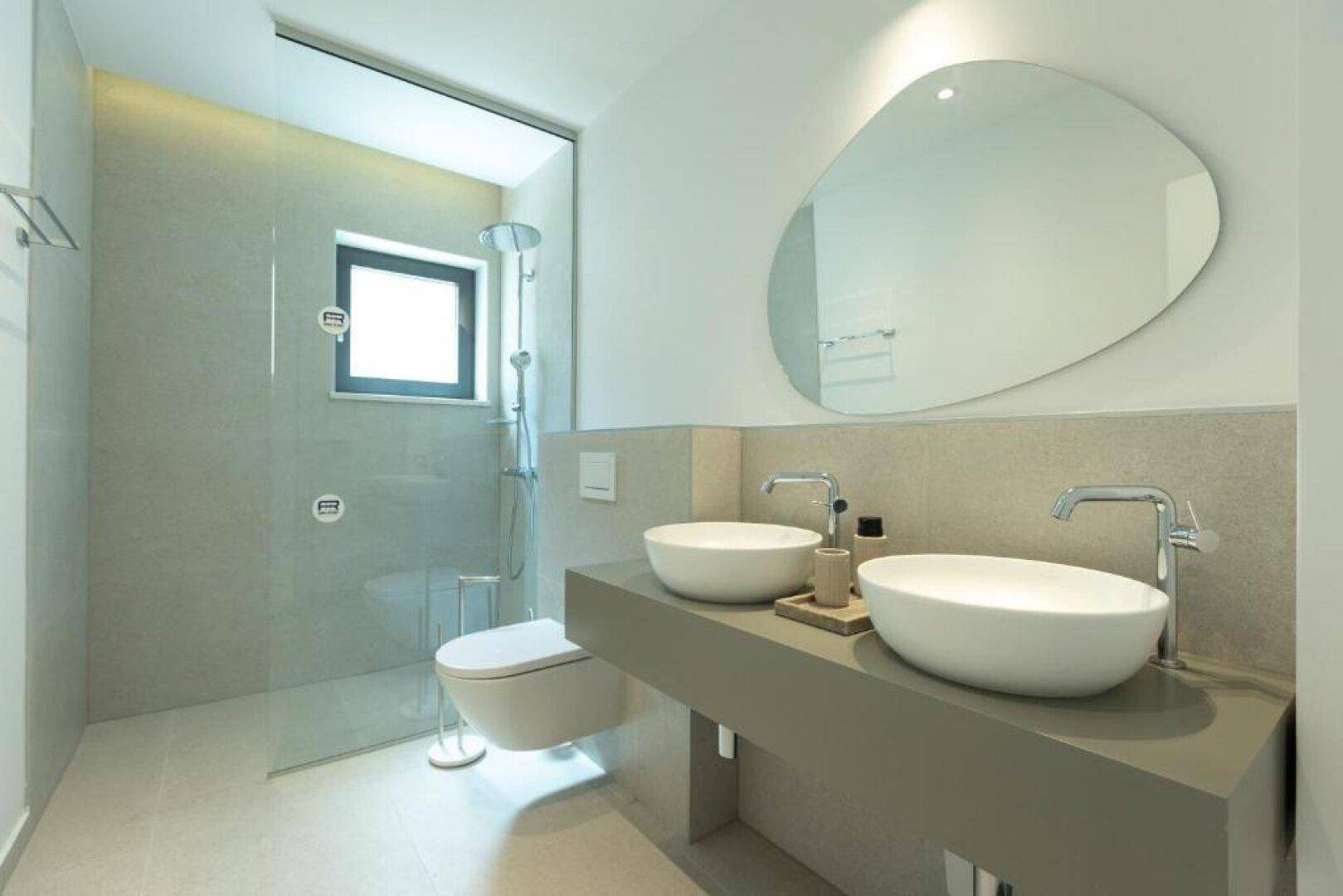 Modernes Badezimmer mit Doppelwaschbecken, begehbarer Dusche und Fenster.