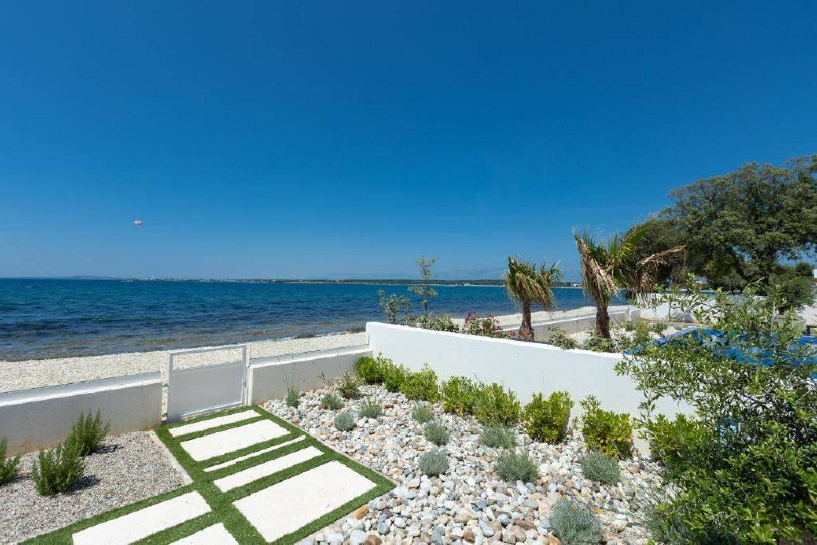 Gepflegter Gartenbereich mit Kies und Pflanzen, der direkt zum Strand und Meer führt.