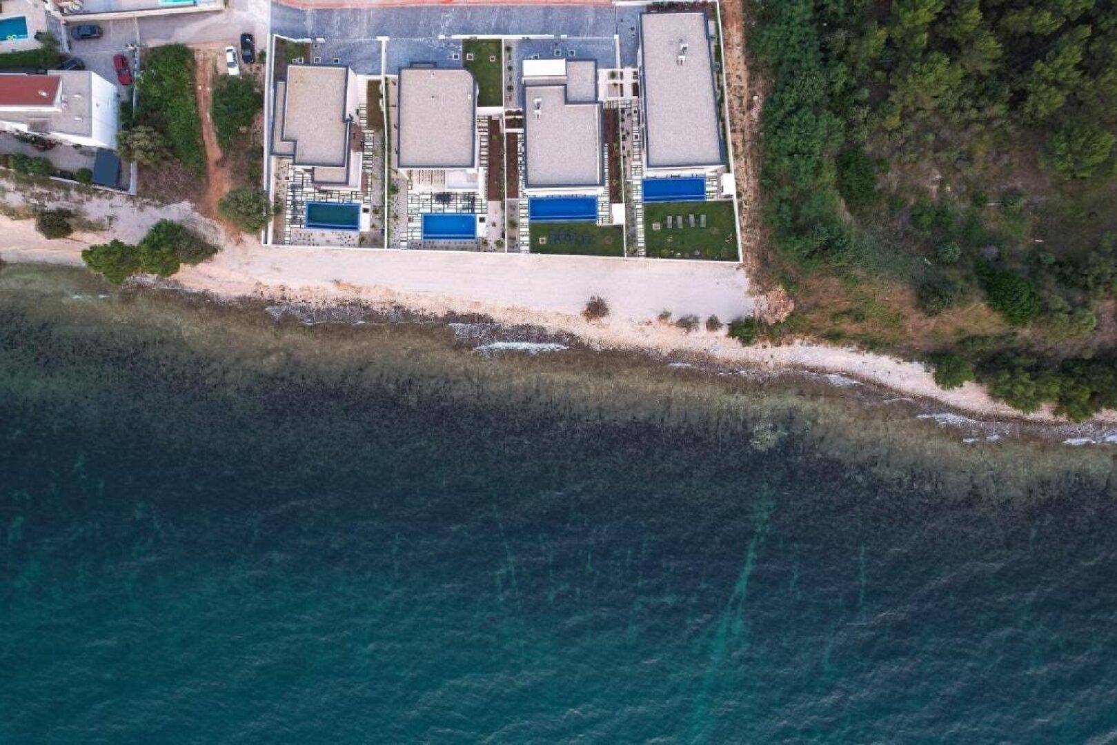Senkrechte Luftaufnahme der Küstenlinie mit modernen Villen, Pools und dem Meer.