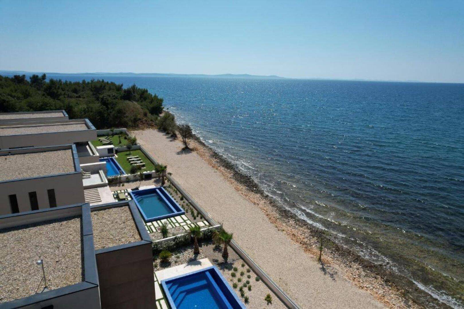 Luftaufnahme der Villenreihe direkt am Strand mit Pools und dem klaren Meer.