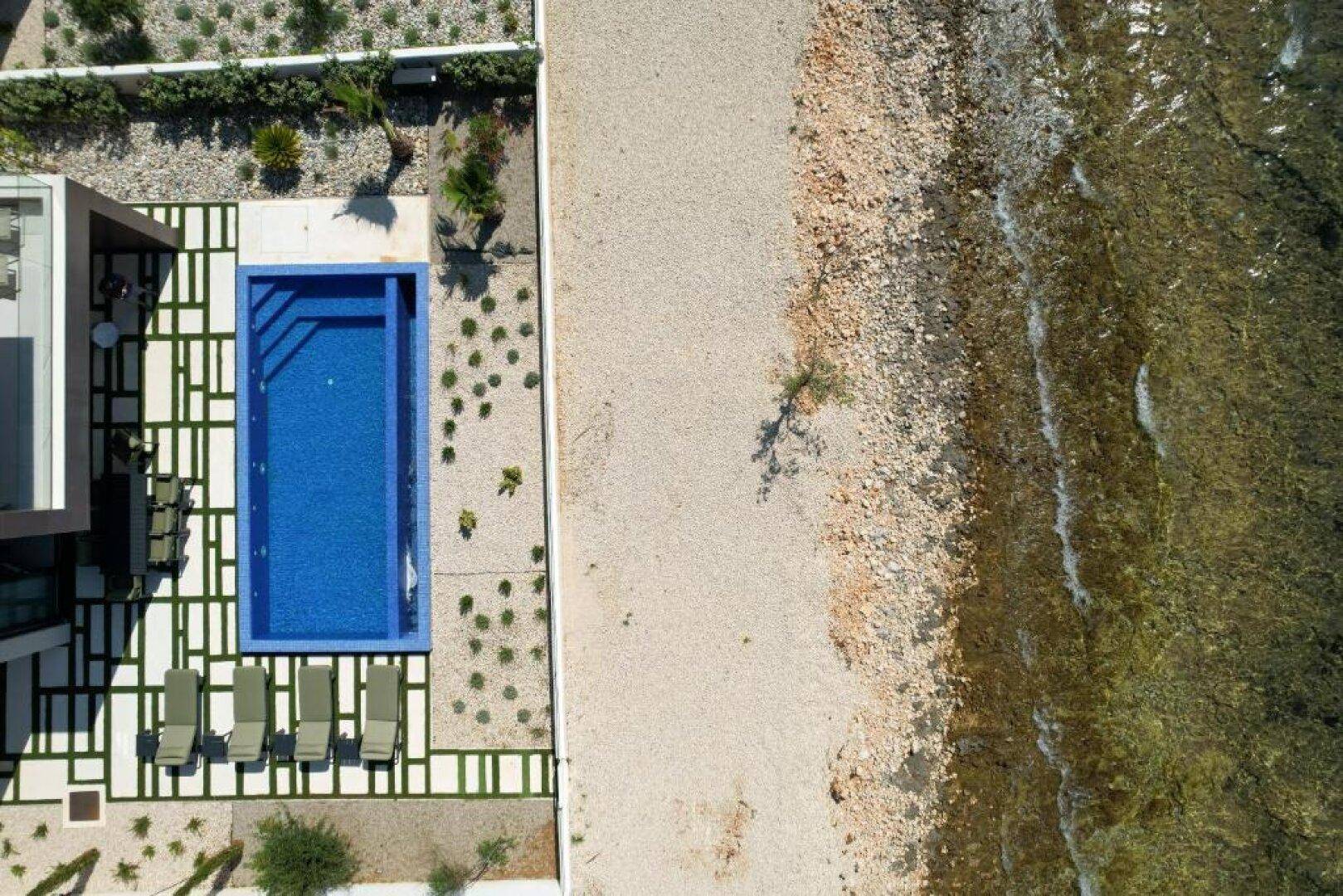 Top-Down-Ansicht eines Pools und des geometrisch gestalteten Gartens am Strand.