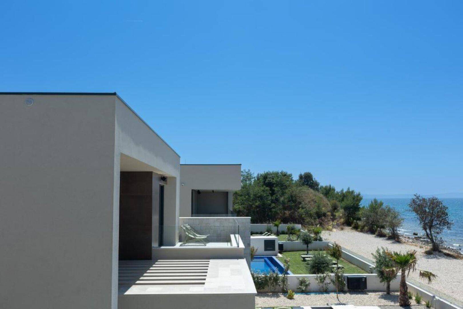 Moderne Villa mit Balkon und Blick auf das Meer, umgeben von mediterraner Vegetation.