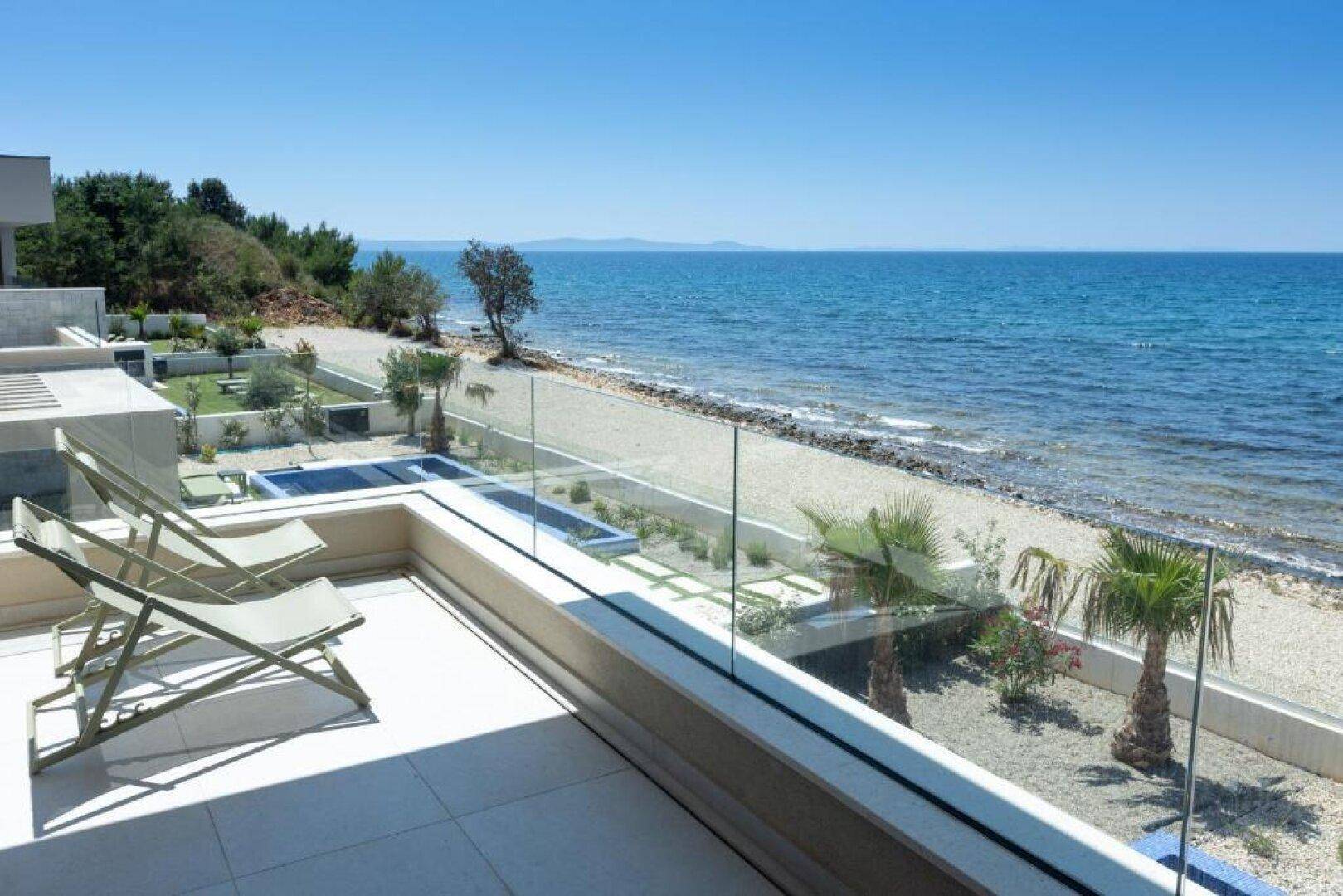 Geräumiger Balkon mit Liegestühlen und Glasgeländer, bietet einen weiten Blick auf das Meer.