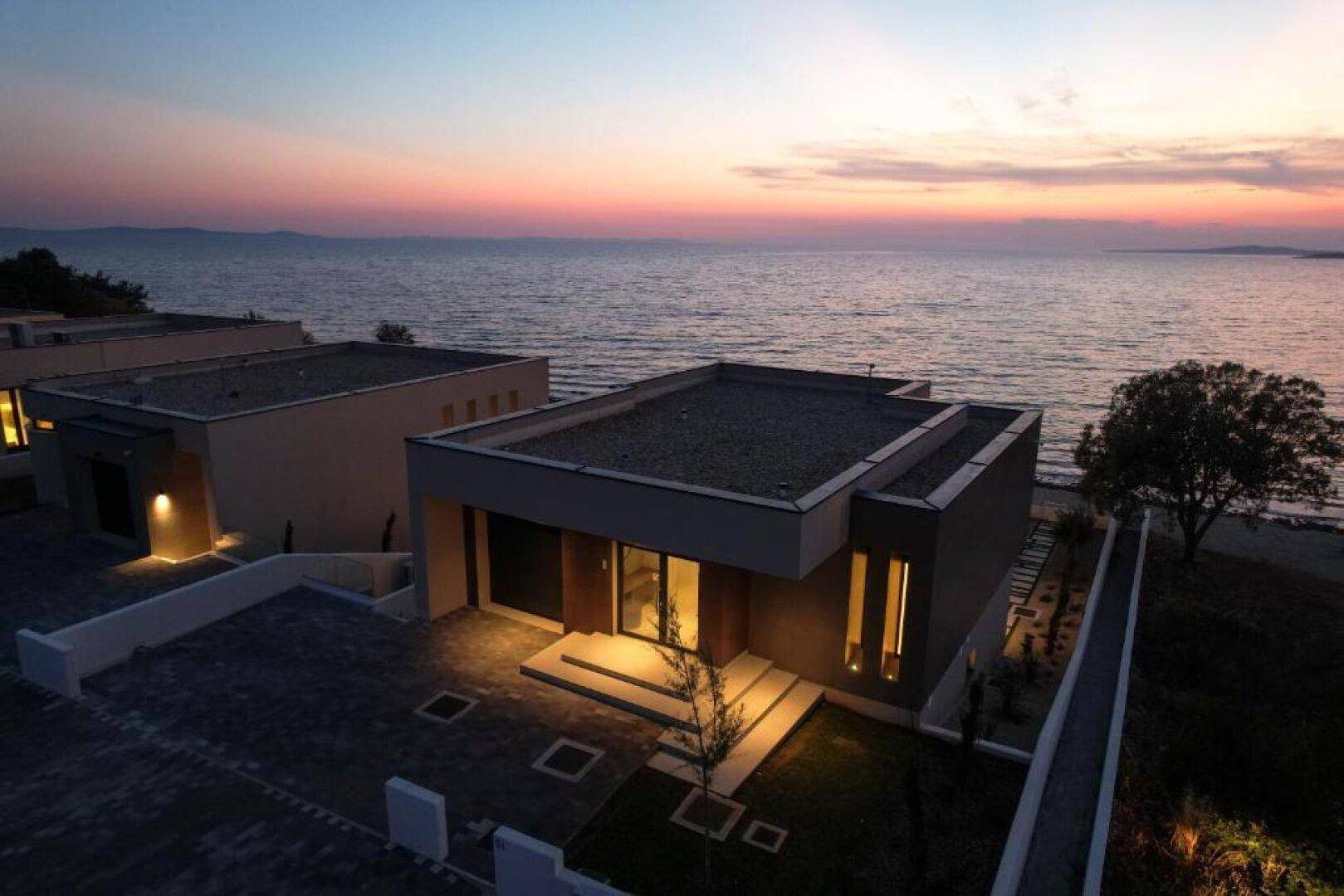 Luftaufnahme einer modernen eingeschossigen Villa bei Sonnenuntergang, mit Meerblick und gepflegter Außenanlage.