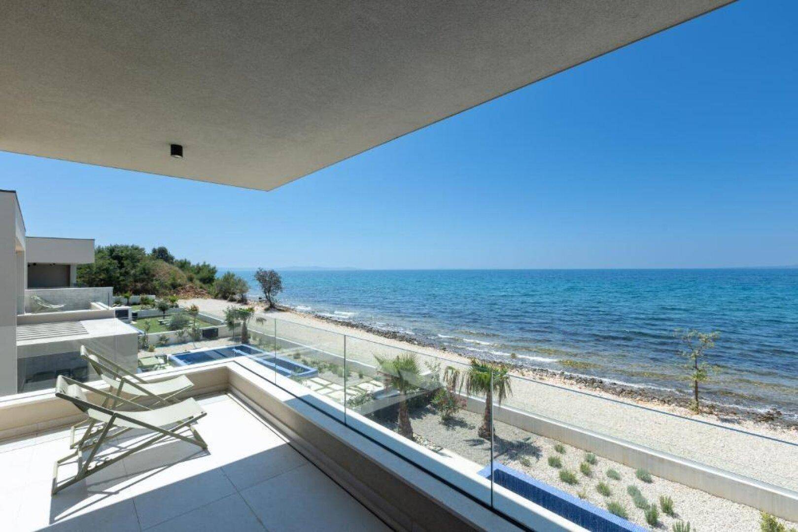 Heller Balkon mit Liegestühlen und Glasgeländer, bietet einen weiten Blick auf das azurblaue Meer.