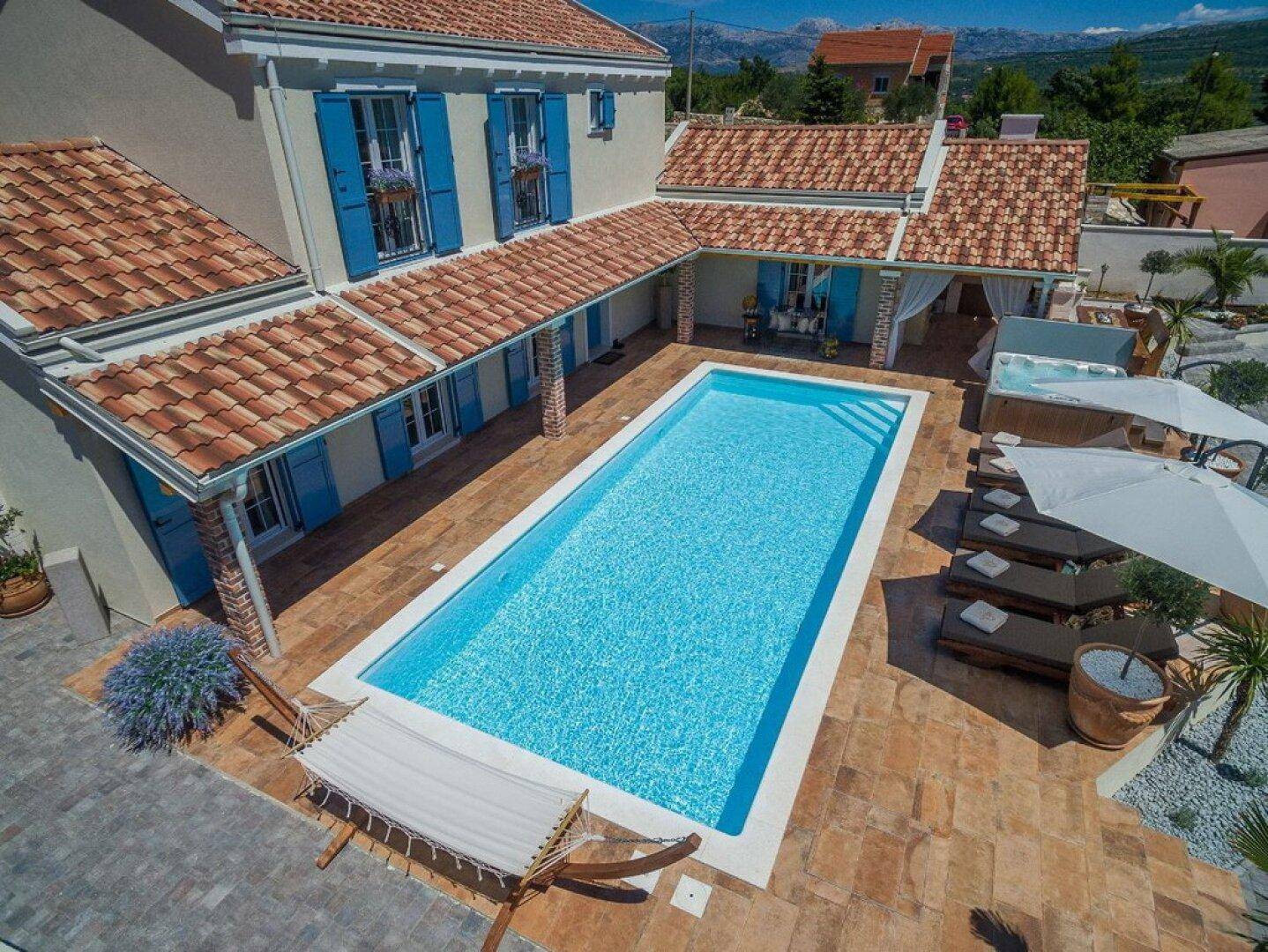 Panoramablick von oben auf die weitläufige Poollandschaft mit Sonnenliegen und dem Hauptgebäude der Villa.