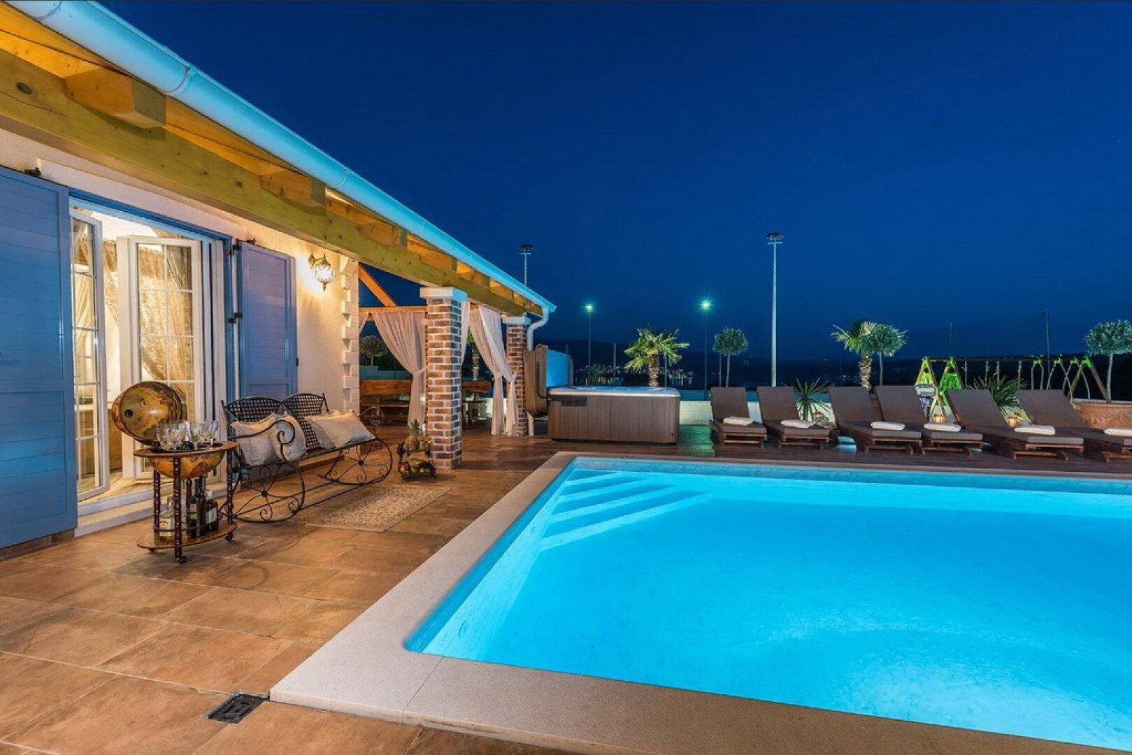 Stimmungsvoll beleuchtete Terrasse am Abend mit Pool, Whirlpool und gemütlichen Sitzgelegenheiten.