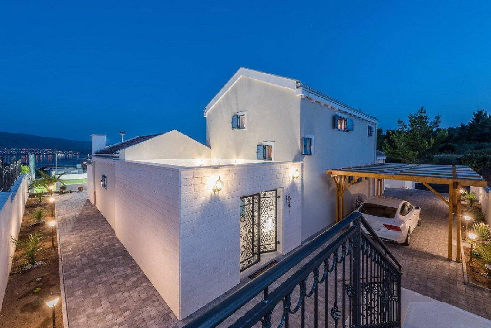 Beleuchtete Zufahrt zur Villa bei Nacht mit Carport und modernem Eingangsbereich.