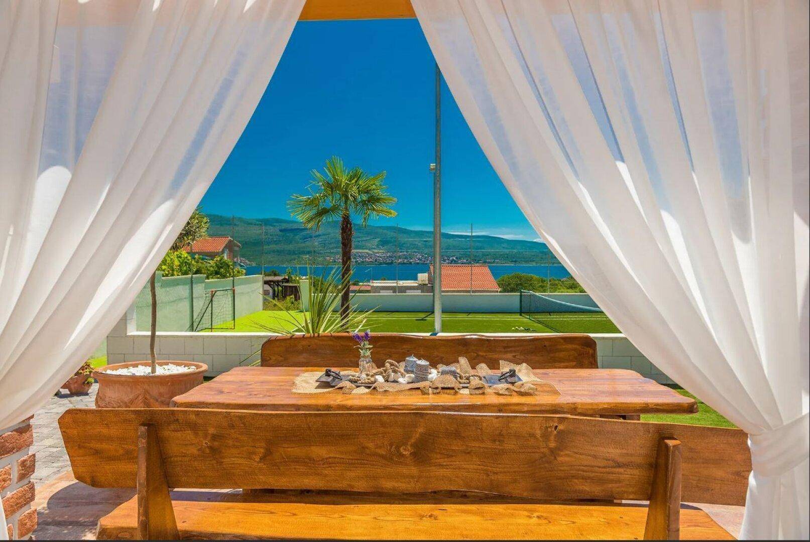 Überdachter Essbereich im Freien mit rustikalem Holztisch und weitem Blick auf das Meer und die Landschaft.