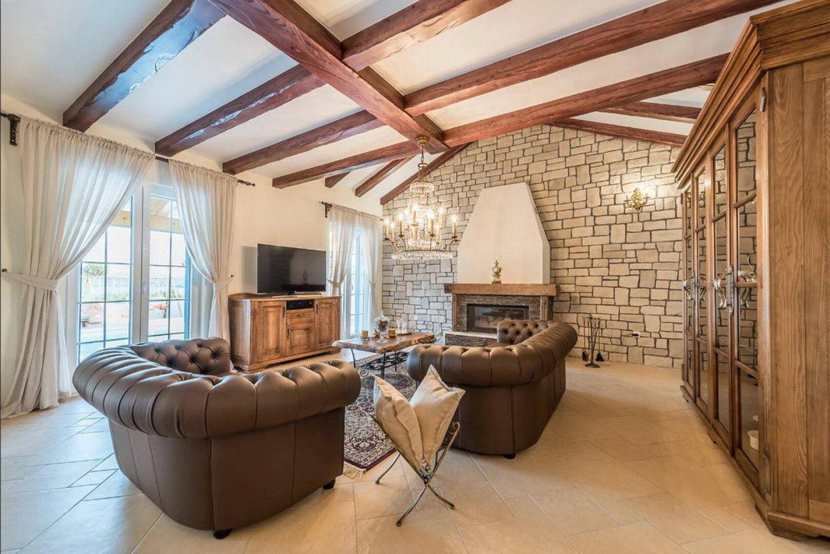 Gemütliches Wohnzimmer mit sichtbaren Holzbalken, Steinkamin und bequemen Ledersofas.