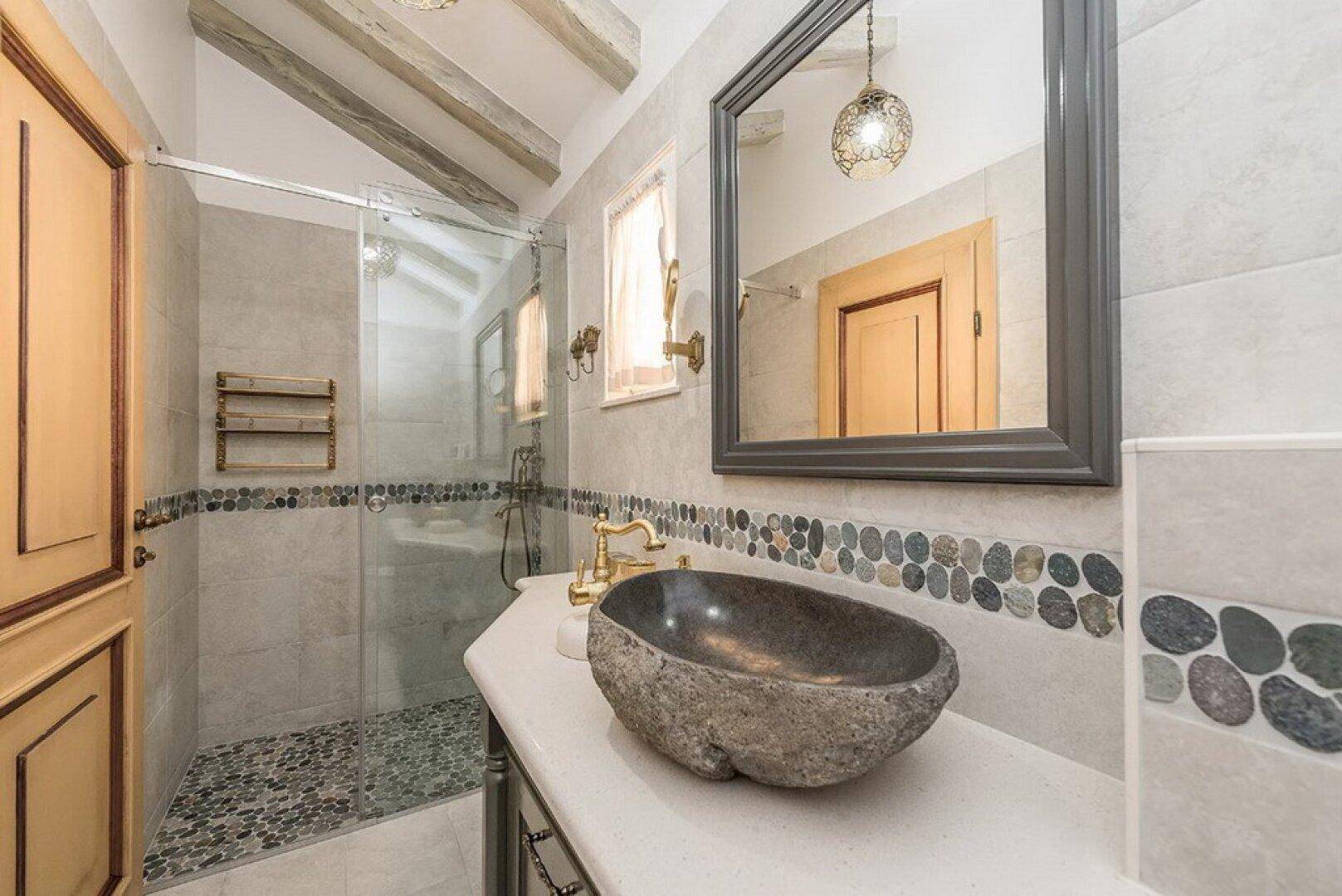Modernes Badezimmer mit Natursteinwaschbecken, begehbarer Dusche und dekorativen Kieselsteinfliesen.