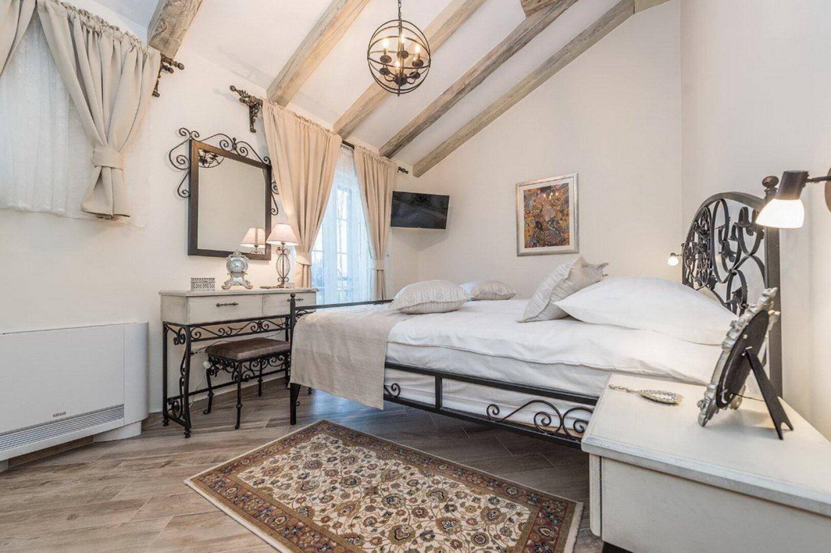 Schlafzimmer mit schmiedeeisernem Bett, Schminktisch und Holzbalkendecke, hell und einladend gestaltet.