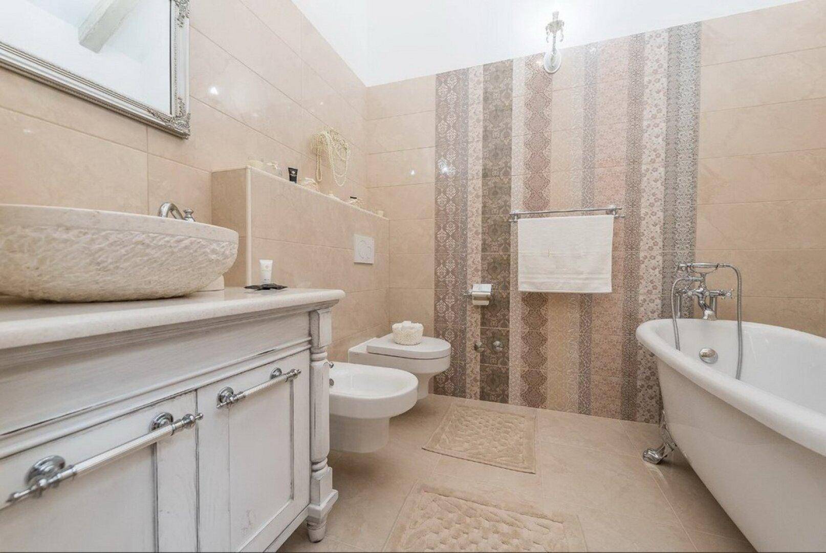 Luxuriöses Badezimmer mit freistehender Badewanne, Bidet und eleganten Fliesen in warmen Farbtönen.