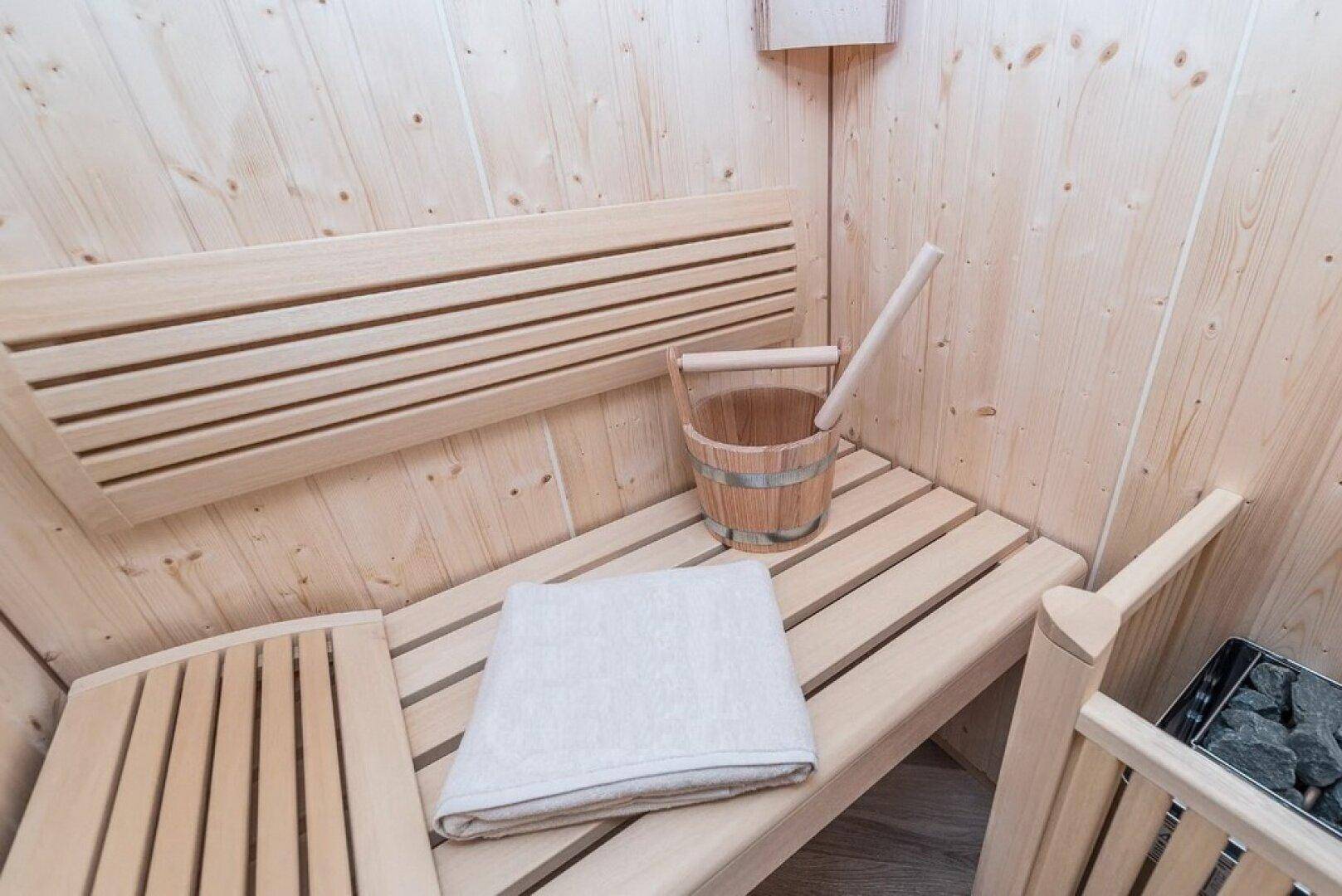 Helle Holzsauna mit traditionellen Bänken und einem Aufgusseimer für entspannende Momente.