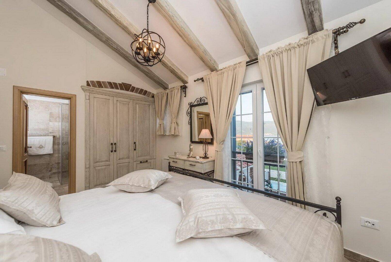 Schlafzimmer mit schmiedeeisernem Bett, Einbauschrank und Holzbalkendecke, mit Zugang zum Badezimmer.