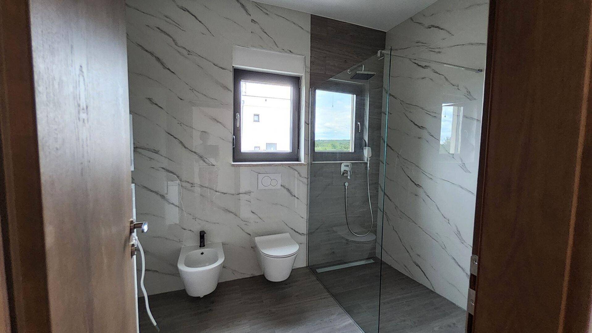 Modernes Badezimmer mit Marmorfliesen, ebenerdiger Dusche, Bidet und Fenster.