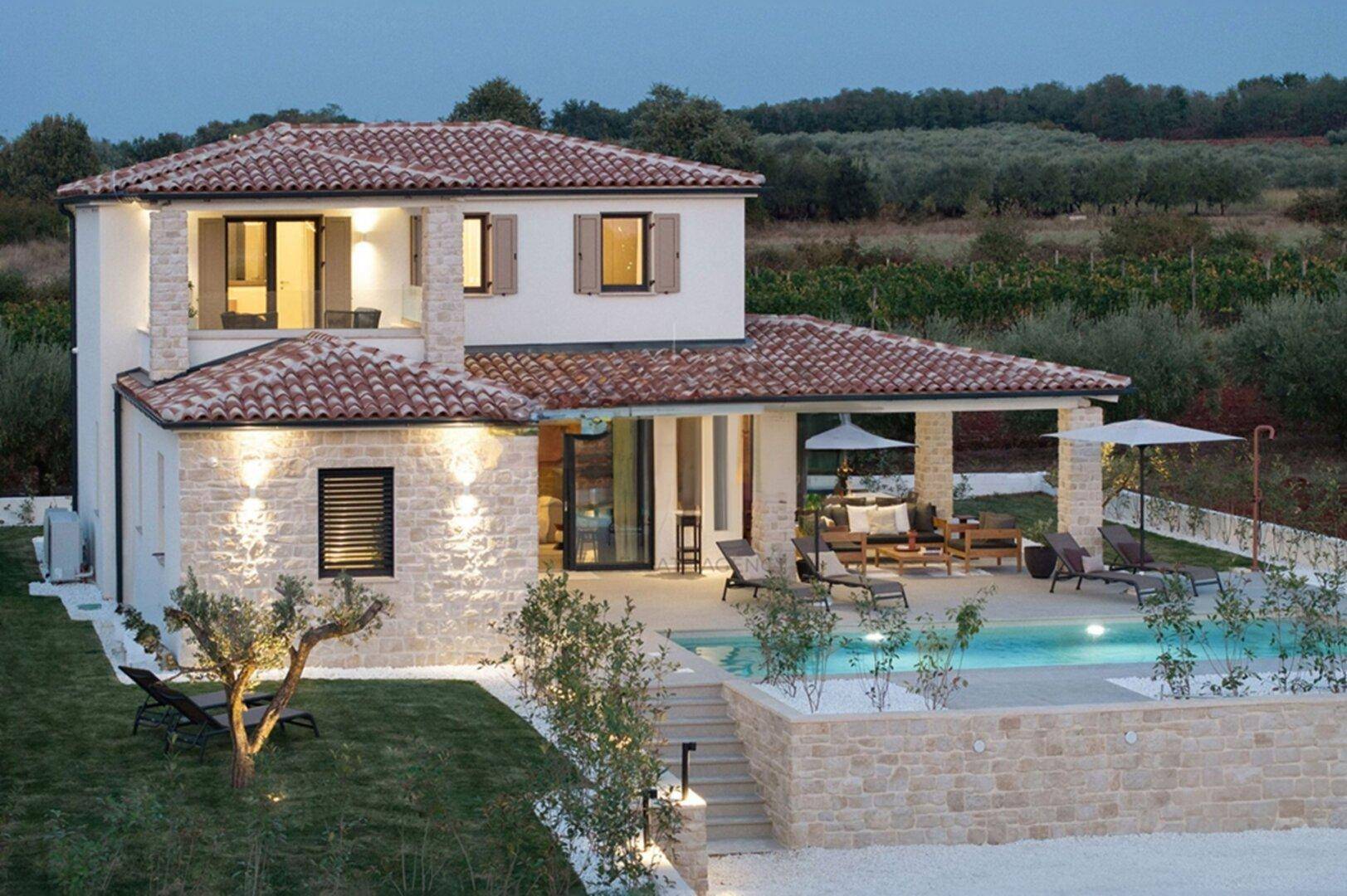 Moderne Villa mit Pool, Steinfassade und mediterraner Umgebung bei Sonnenuntergang.