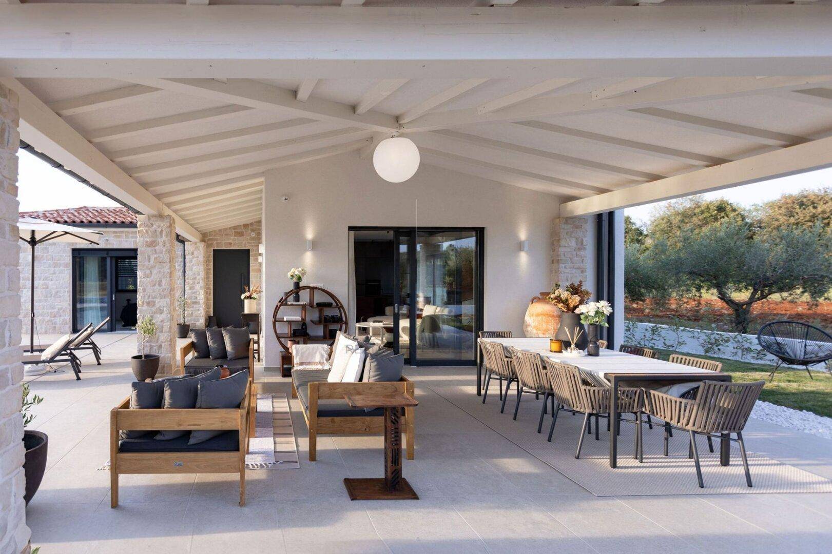 Geräumige überdachte Terrasse mit Essbereich und Lounge-Möbeln, umgeben von Natur.