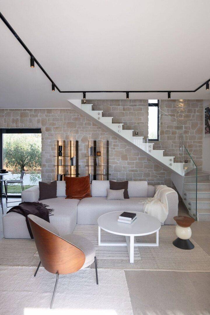Stilvolles Wohnzimmer mit bequemer Couch, Steinfassade und moderner Treppe mit Glasgeländer.