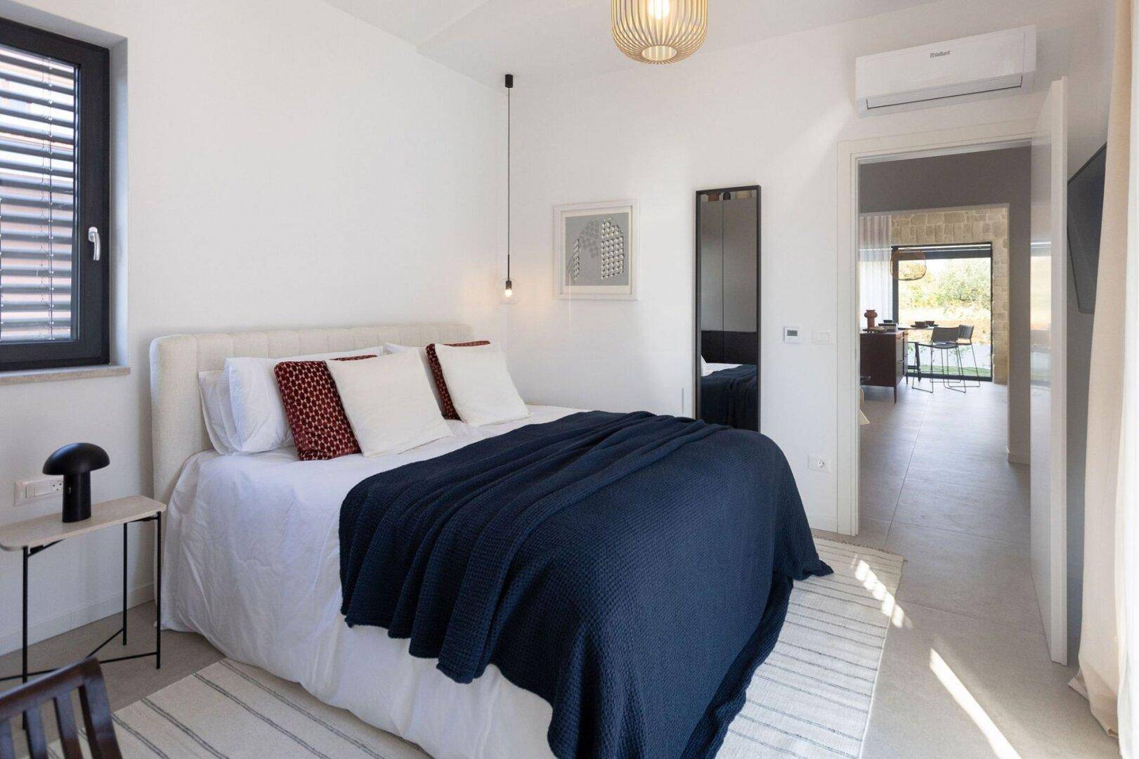 Helles Schlafzimmer mit Doppelbett, Klimaanlage und Blick in den angrenzenden Wohnbereich.