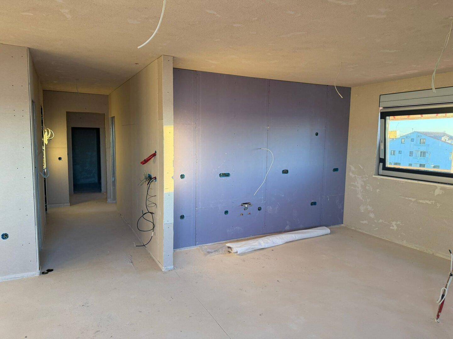 Innenraum im Rohbau mit Trockenbauwänden und vorbereiteten Elektroinstallationen.
