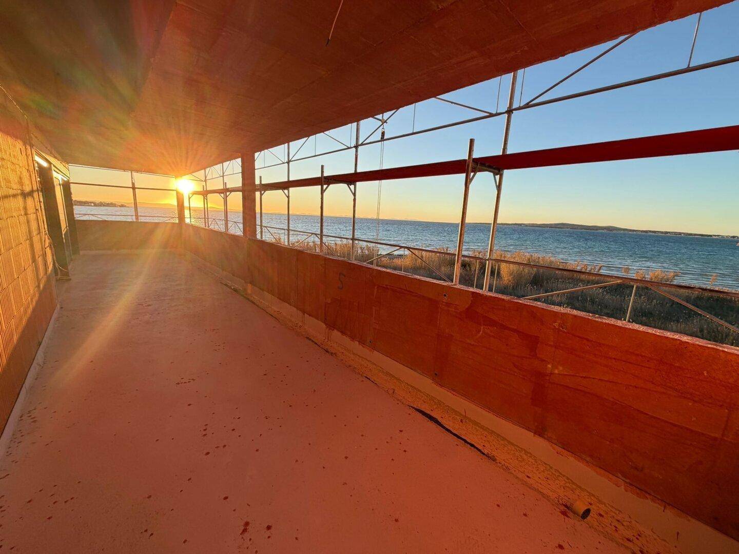 Balkon im Rohbau mit weitem Meerblick bei Sonnenuntergang.