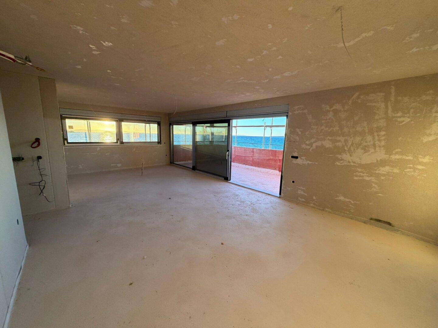 Geräumiger Wohnbereich im Rohbau mit großen Schiebetüren und Meerblick.