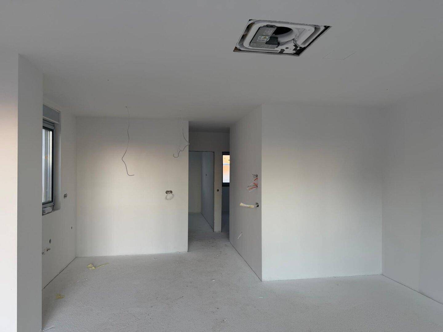Unfertiger Innenraum mit weißen Wänden, Rohbau und sichtbaren Elektroinstallationen während der Bauphase.