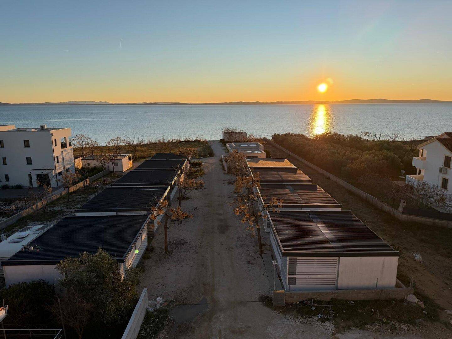 Reihen von Gebäuden in Küstennähe mit Blick auf das Meer bei Sonnenuntergang und klarem Himmel.