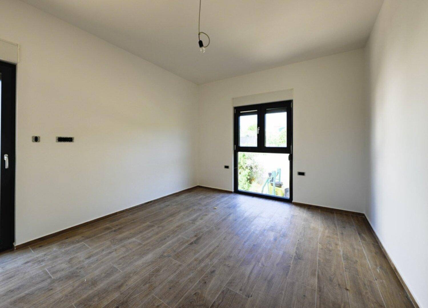 Leerer Raum mit Holzoptik-Fliesenboden und Zugang zu einem kleinen Balkon oder Garten.