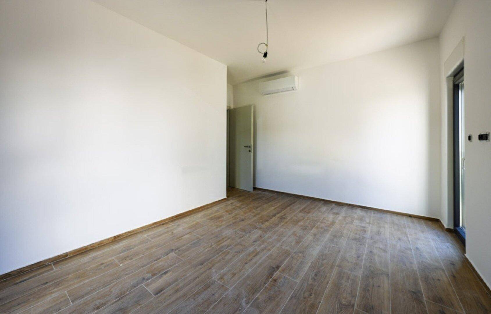 Heller, unmöblierter Raum mit Klimaanlage und modernem Fliesenboden in Holzoptik.