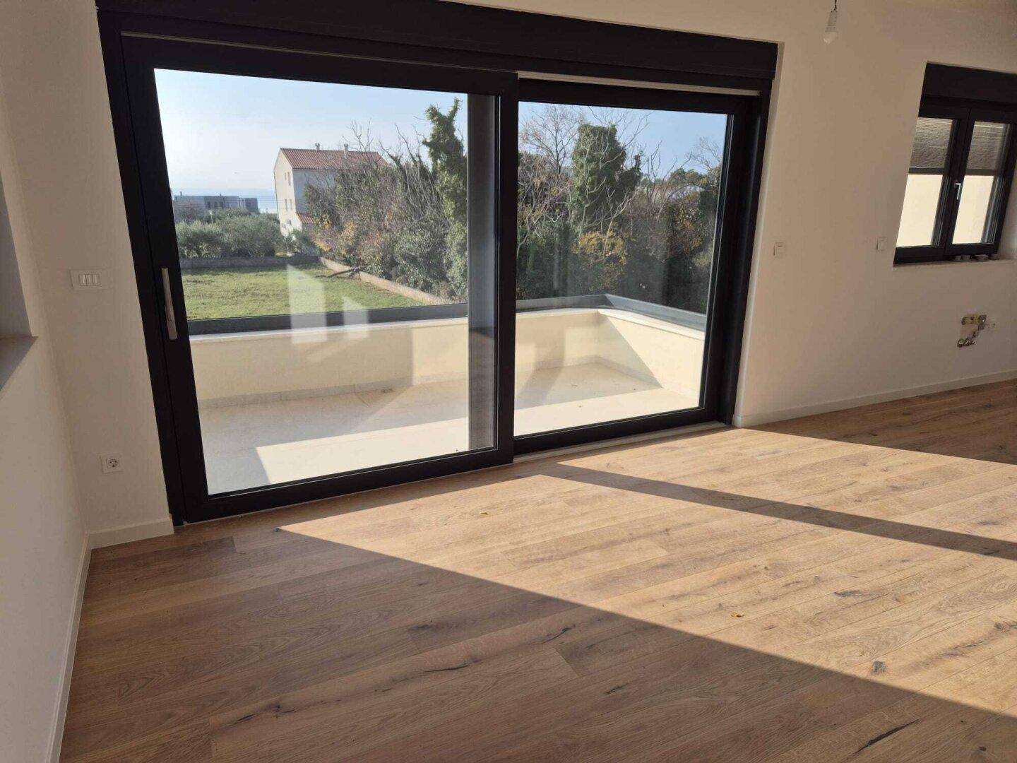 Heller Raum mit Holzboden und großen Schiebetüren, die auf eine Terrasse führen.