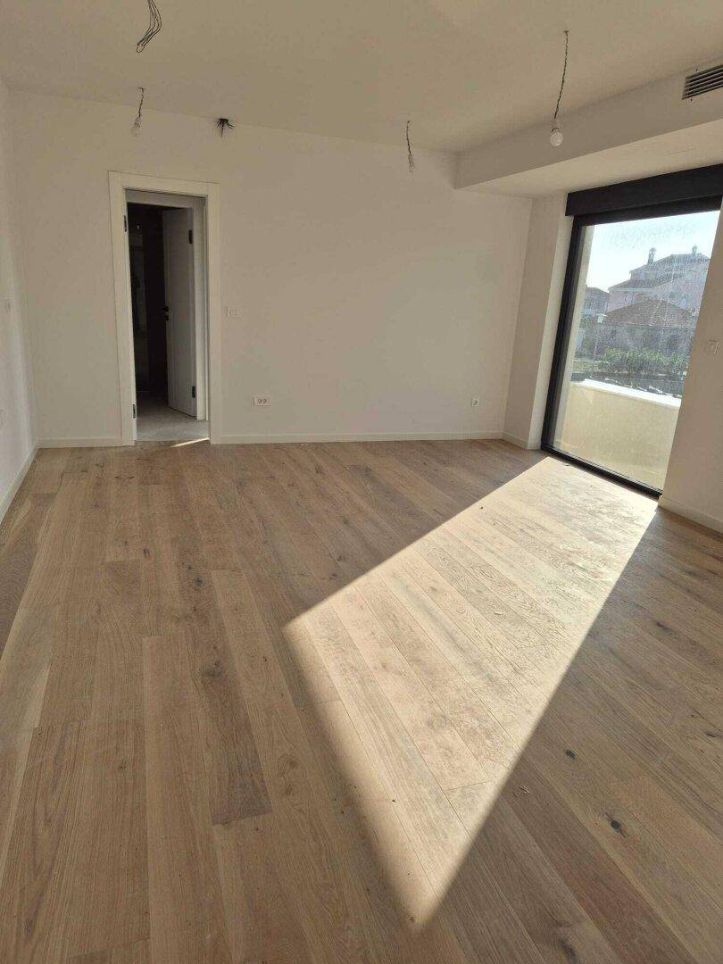Leeres Schlafzimmer mit Holzboden und großem Fenster, das viel Tageslicht hereinlässt.