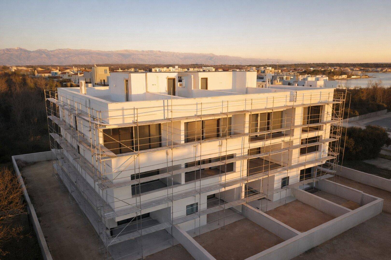 Neubau eines Apartmentgebäudes mit Gerüst, umgeben von einer Küstenlandschaft.